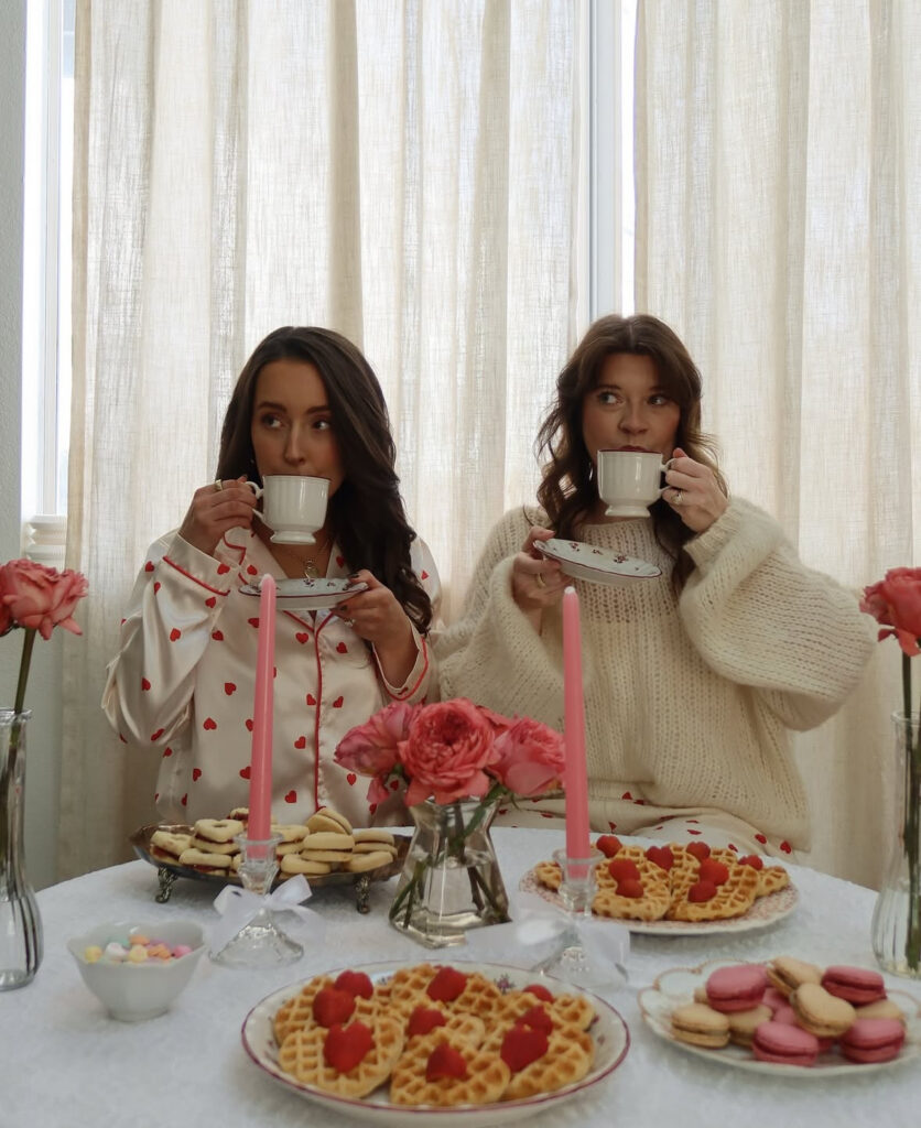Two women enjoying brunch outfits for Galentine’s Day while holding drinks at a decorated table