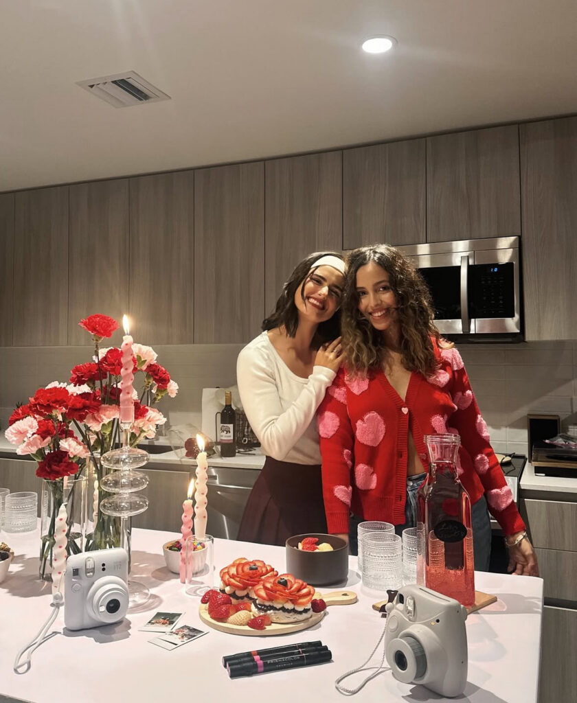 Two women in red and pink Galentine’s outfits celebrating with desserts and drinks at home