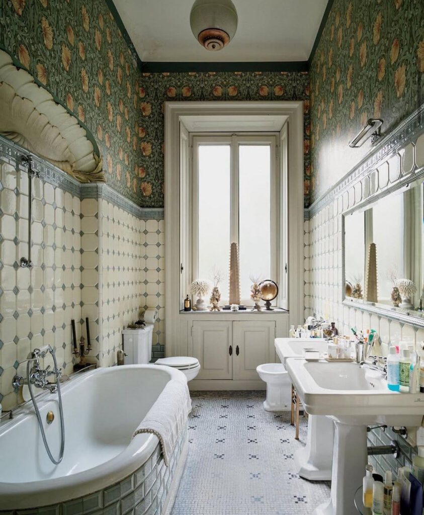 High-ceilinged European-style room wrapped in patterned vintage bathroom tile with pedestal sinks and tub.