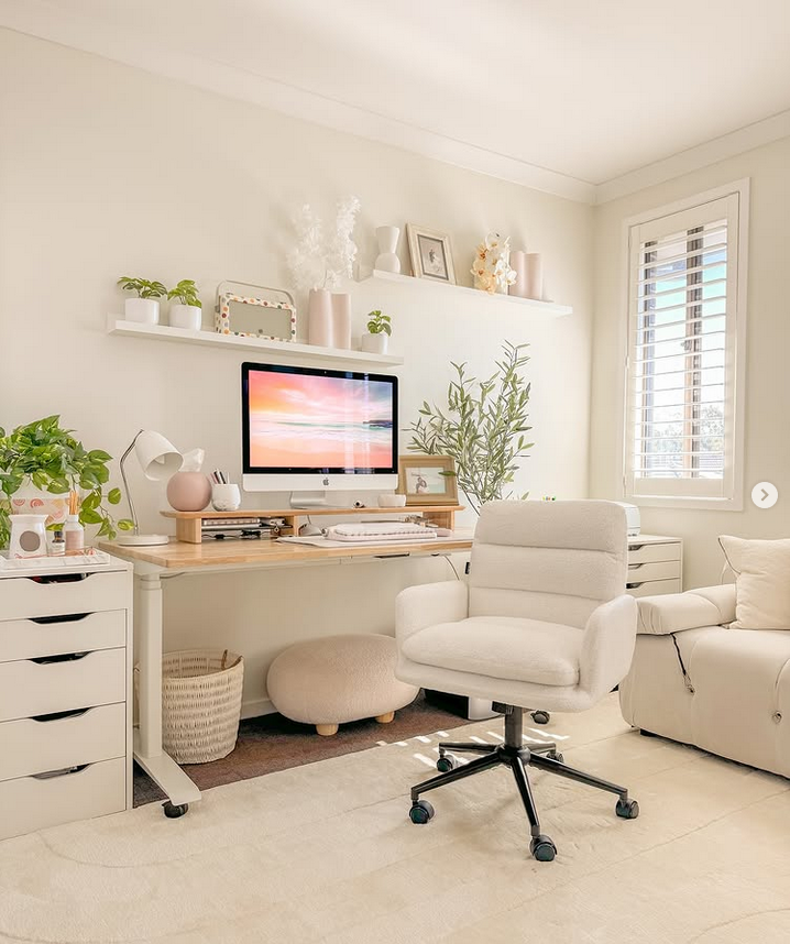 Cream-toned home office with a plush swivel chair, floating shelves, soft decor, and light wood accents.