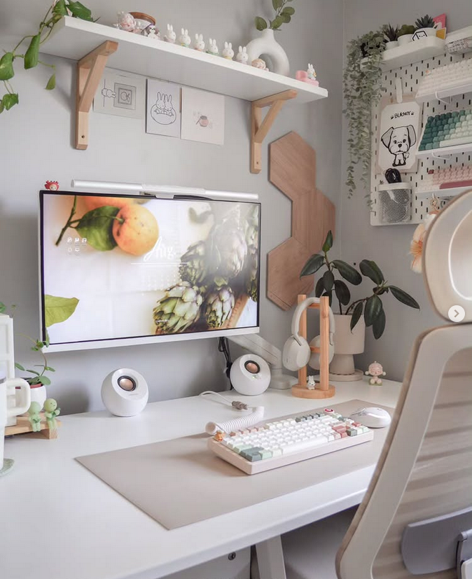 White desk setup with a pegboard organizer, cute decor on shelves, plants, and a pastel keyboard.