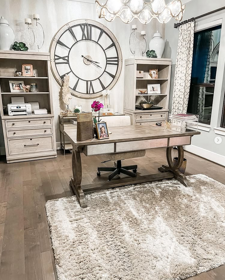 Home office with a giant wall clock, matching storage units, chandelier lighting, and a large textured rug