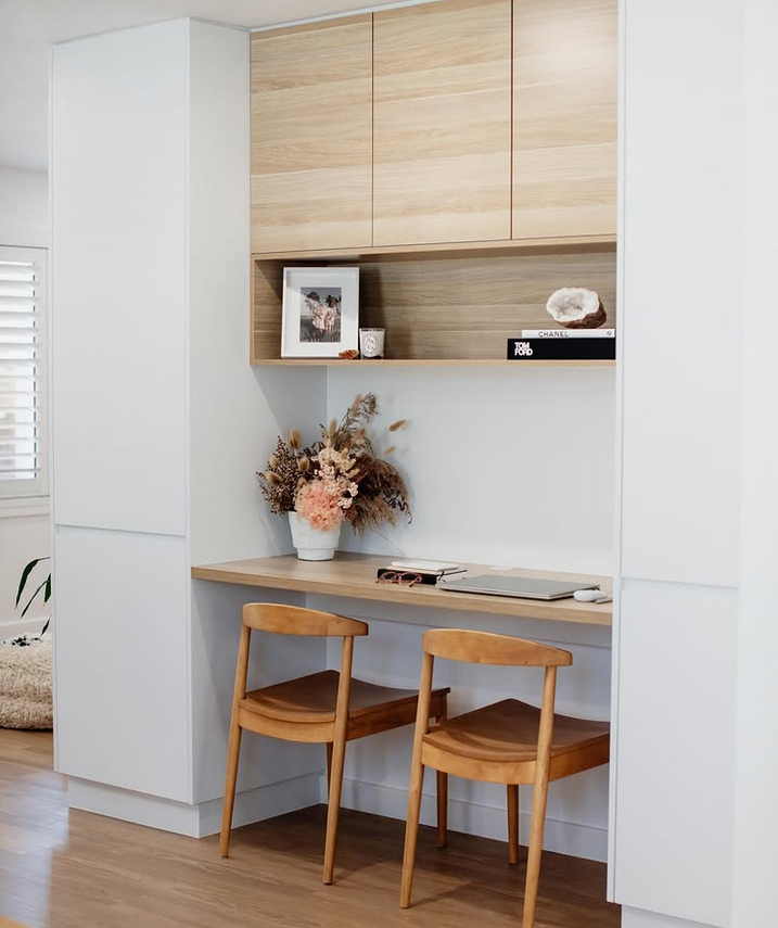 Small office on a landing with built-in shelves, a desk by the window, and a patterned roman shade.