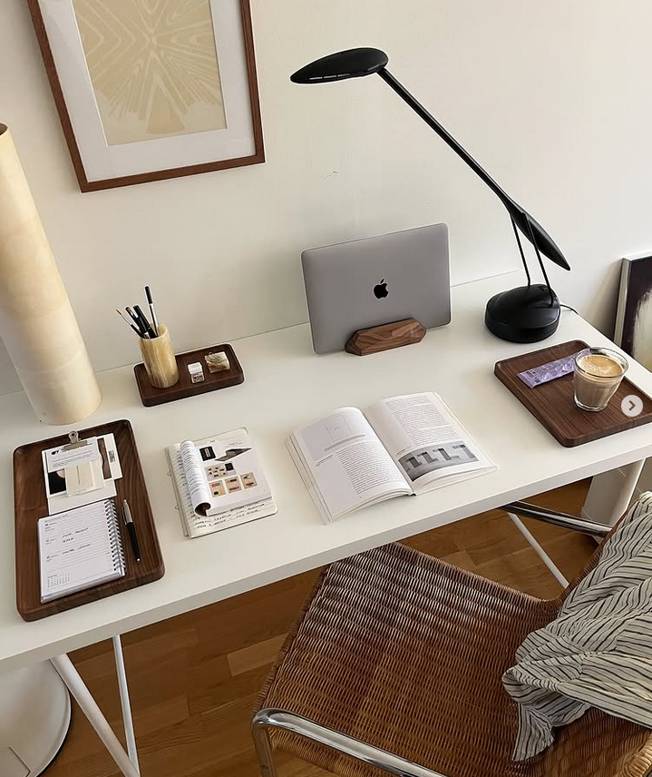 Minimal desk styling with wooden organizer trays, a black task lamp, an open book, and a drink on a tray.
