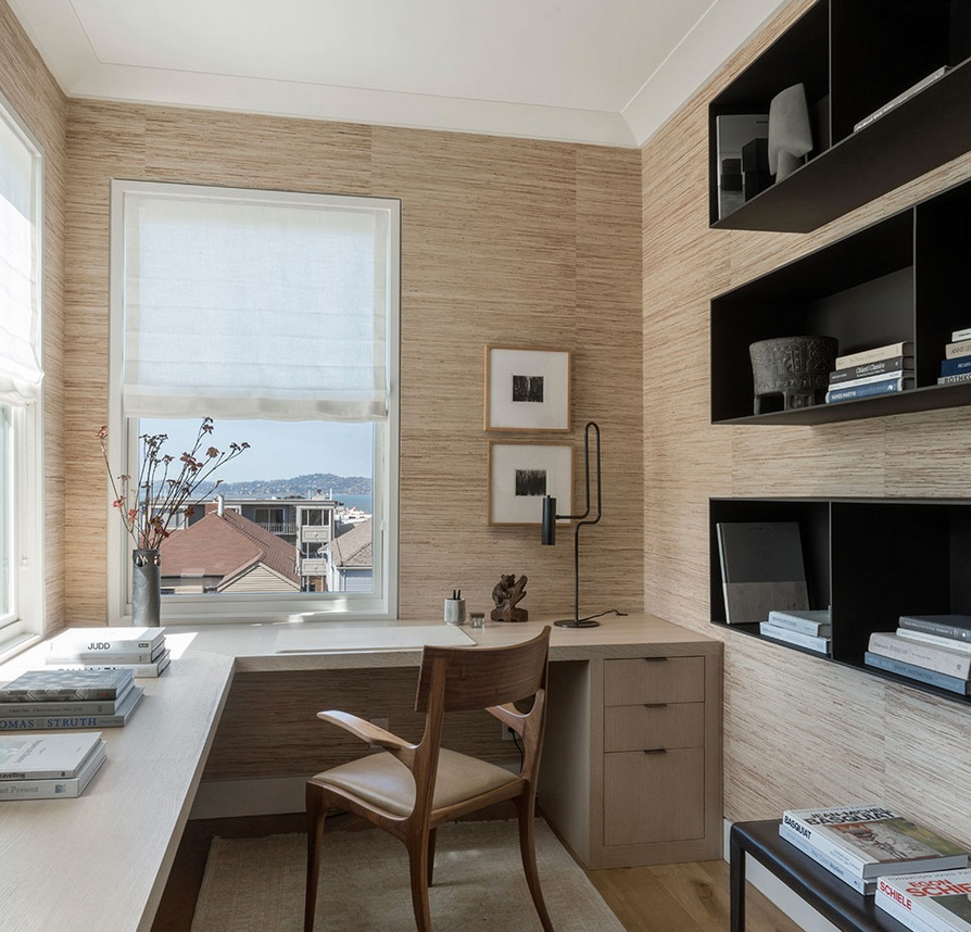 Neutral office with textured wallcovering, black cubby shelves, an L-shaped desk, and a wood chair.