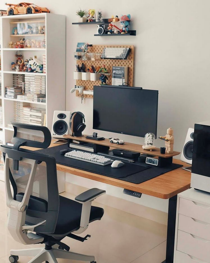 Standing desk setup with an ergonomic chair, large monitor, speakers, and a pegboard wall organizer.