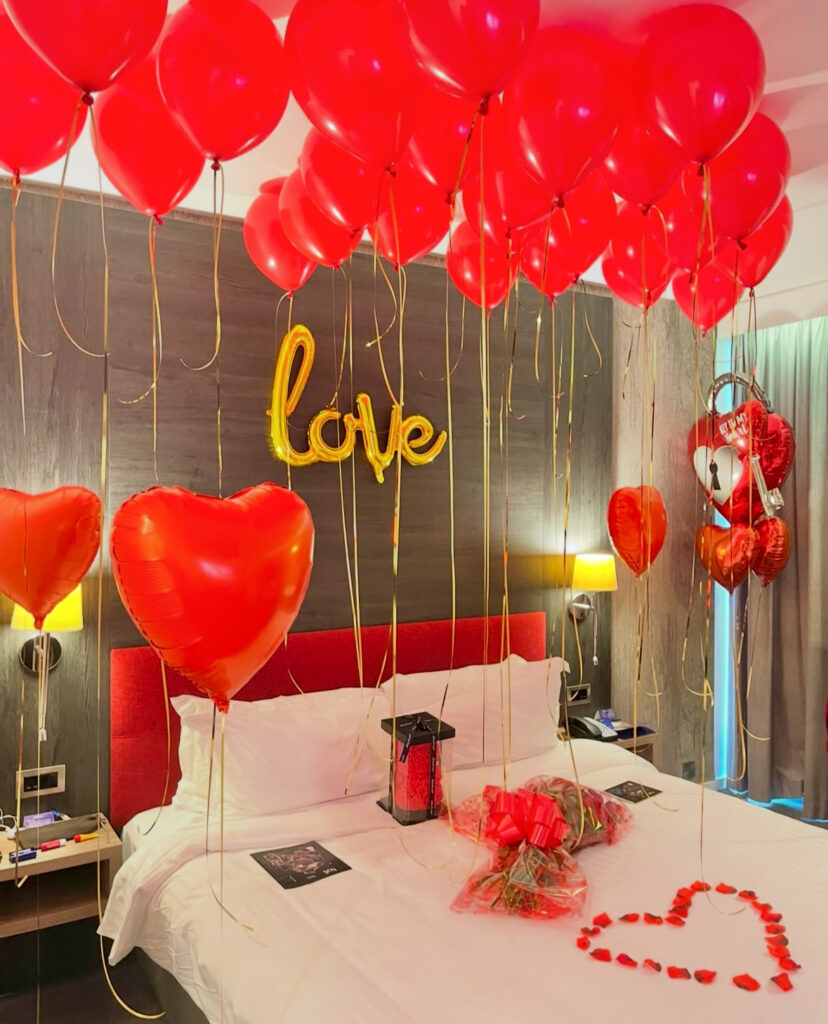 Romantic hotel bedroom filled with red balloons, golden ribbons, and roses—a dreamy take on romantic bedroom ideas for valentines day.