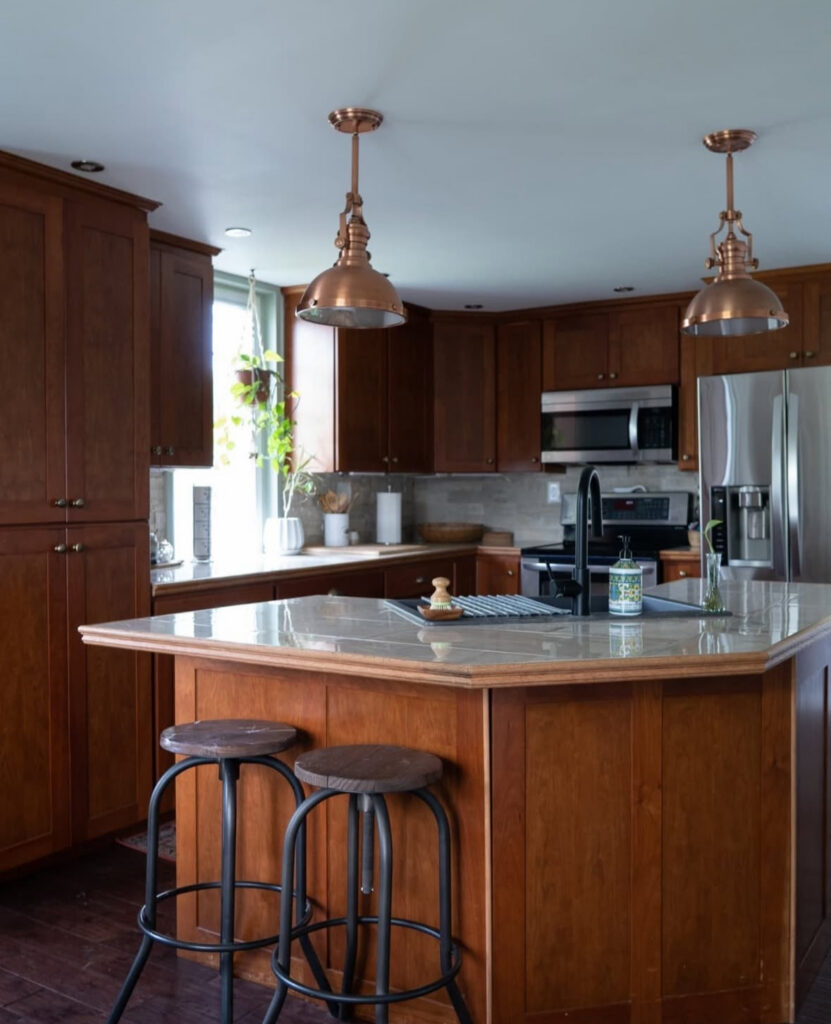 Kitchen with red-toned wood cabinets and a glossy stone island before the charcoal and copper makeover by @diyinprogress_.