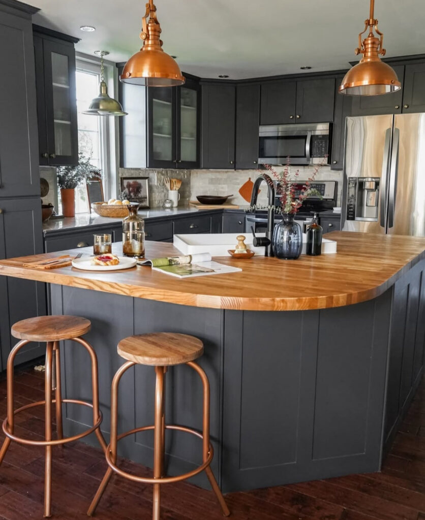 Cosy kitchen with charcoal-painted cabinets, warm wood counters and copper pendants over the island designed by @diyinprogress_.