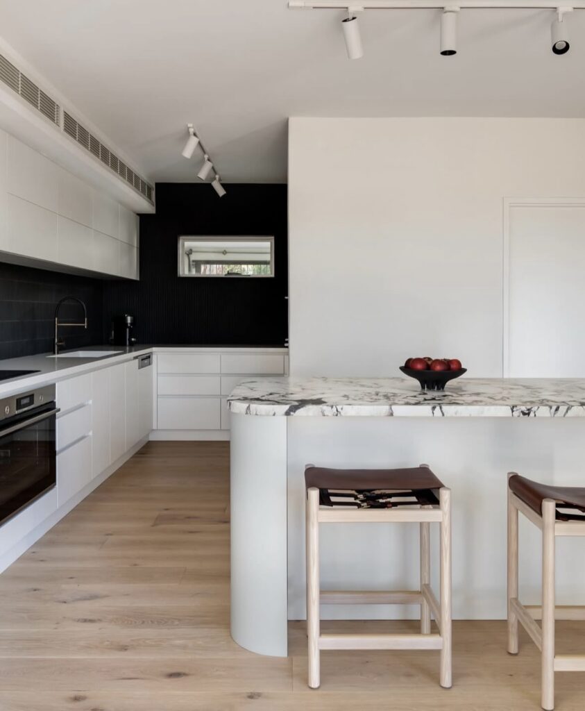 Sleek modern kitchen with a long island, floor-to-ceiling cabinetry, pale timber floors and a black feature wall by @collectedinteriorsperth.