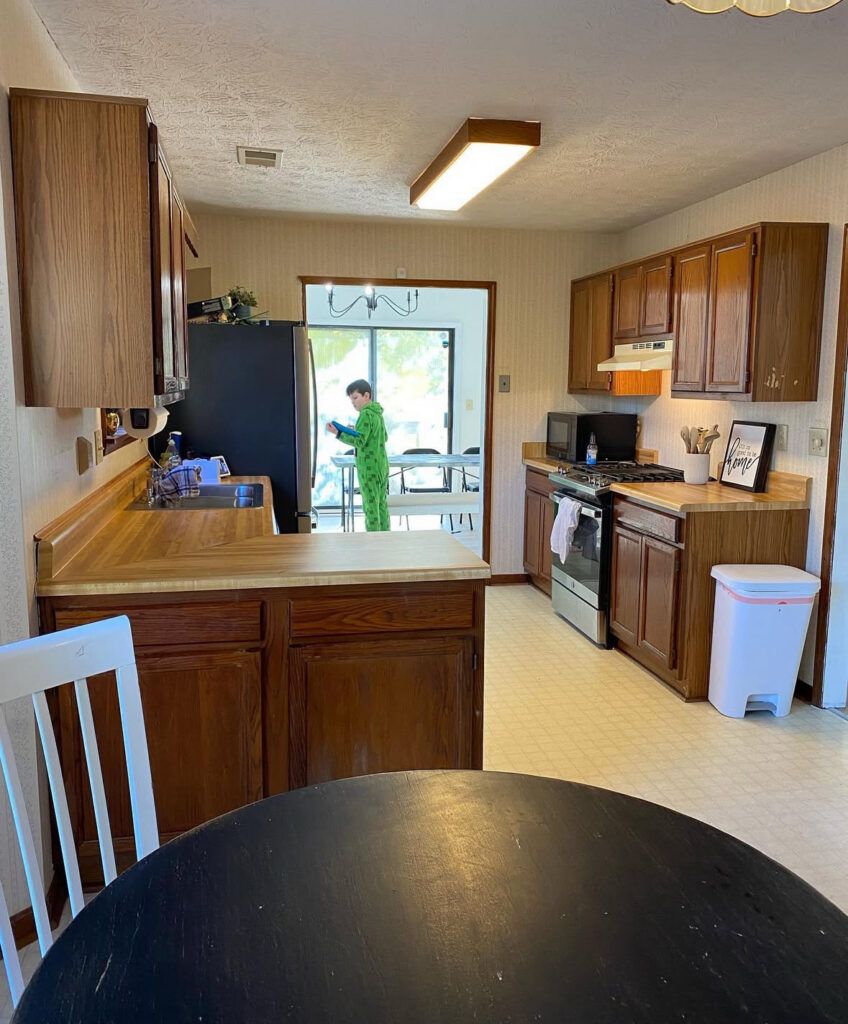 Long galley kitchen with a dated fluorescent ceiling light box and dark cabinets before the new kitchen lighting plan by @delancey.diy.