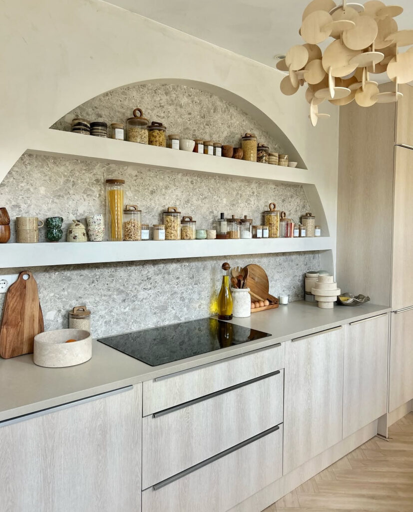 Hetkijkhuis kitchen with arched stone niche, glass jars, and pale oak cabinets, a Scandinavian-inspired interior celebrating beautiful kitchen organization.