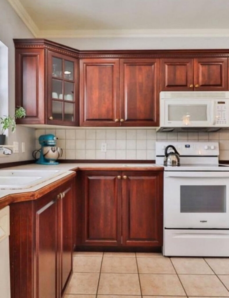 Dark cherry cabinets and beige tile in a dated kitchen before the farmhouse-style kitchen renovation by @designsbykaran.