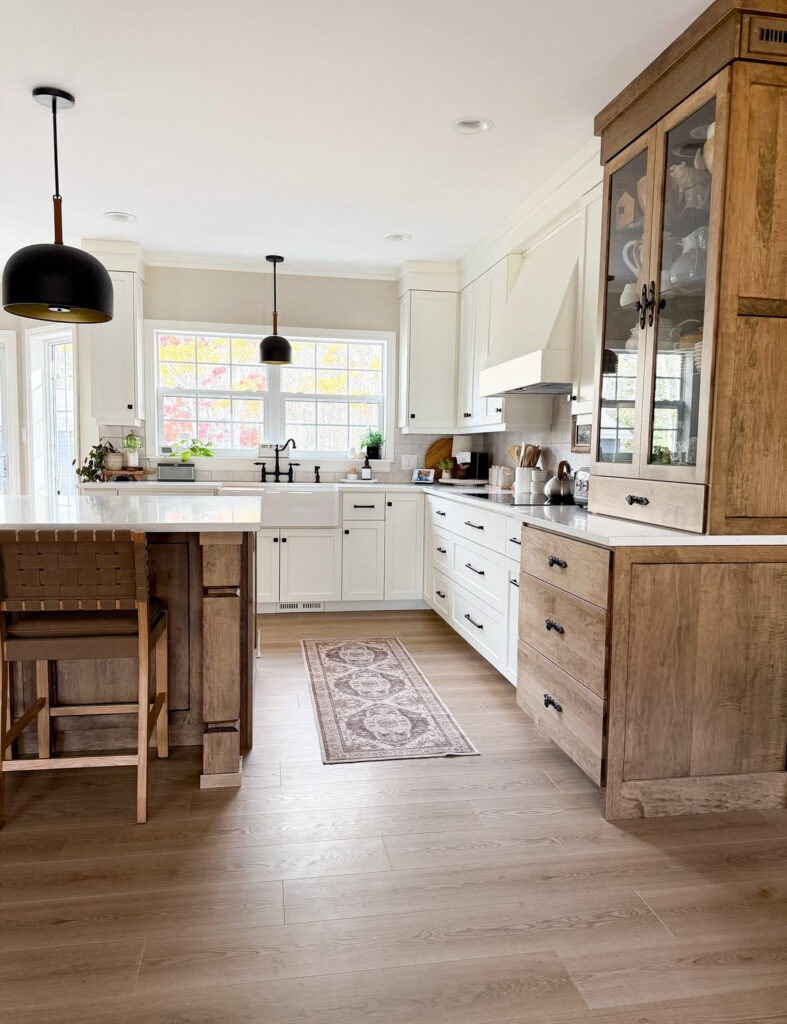 Farmhouse kitchen with white shaker cabinets, pale wood floors, a large island and black accents by @designsbykaran.