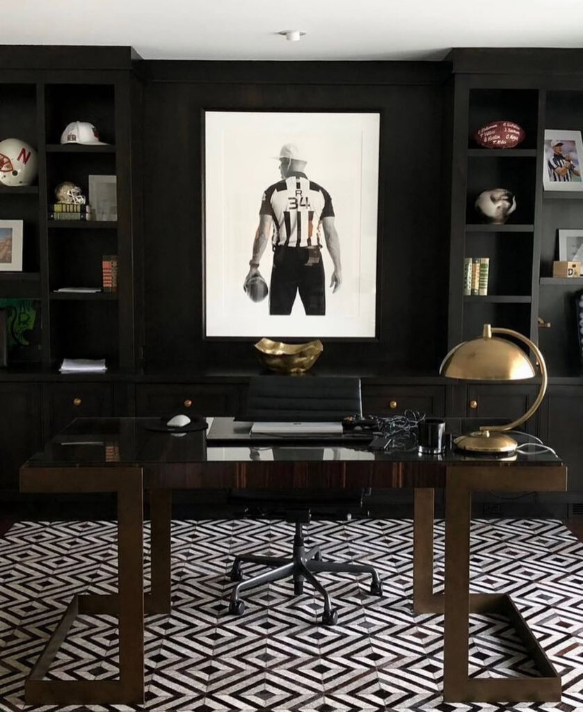 Dark blue masculine office featuring built-in drawers, a curved waterfall desk, tall sculptural desk chair, abstract artwork and a geometric area rug