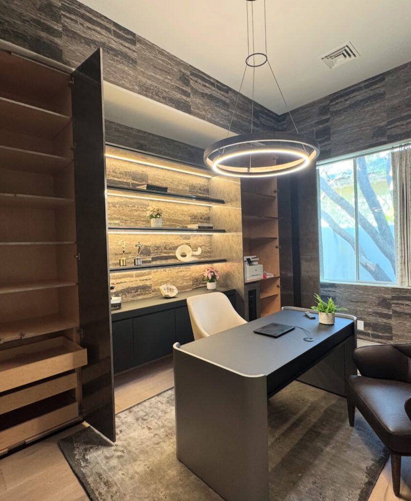 Contemporary masculine office with textured stone-look walls, backlit shelves, streamlined desk with rounded corners, leather lounge chair and a large circular ring pendant