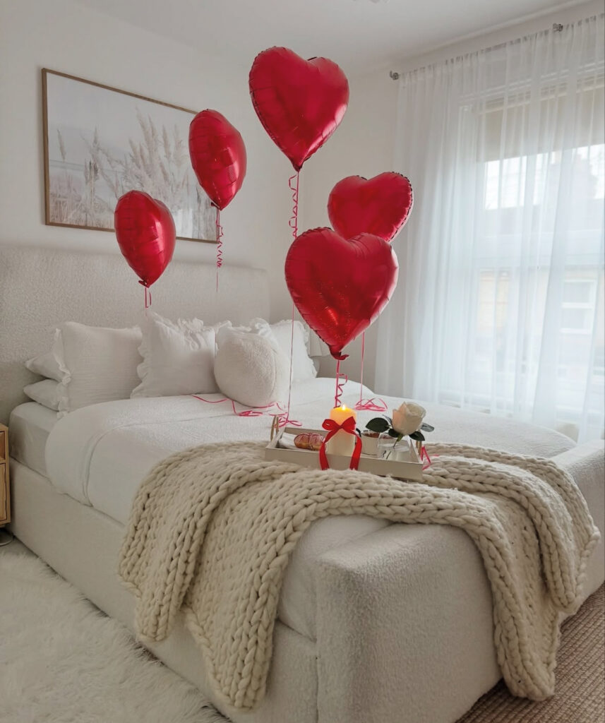 Minimalist white bedroom with red heart balloons and a breakfast tray showing how to decorate a bedroom for valentines day softly.