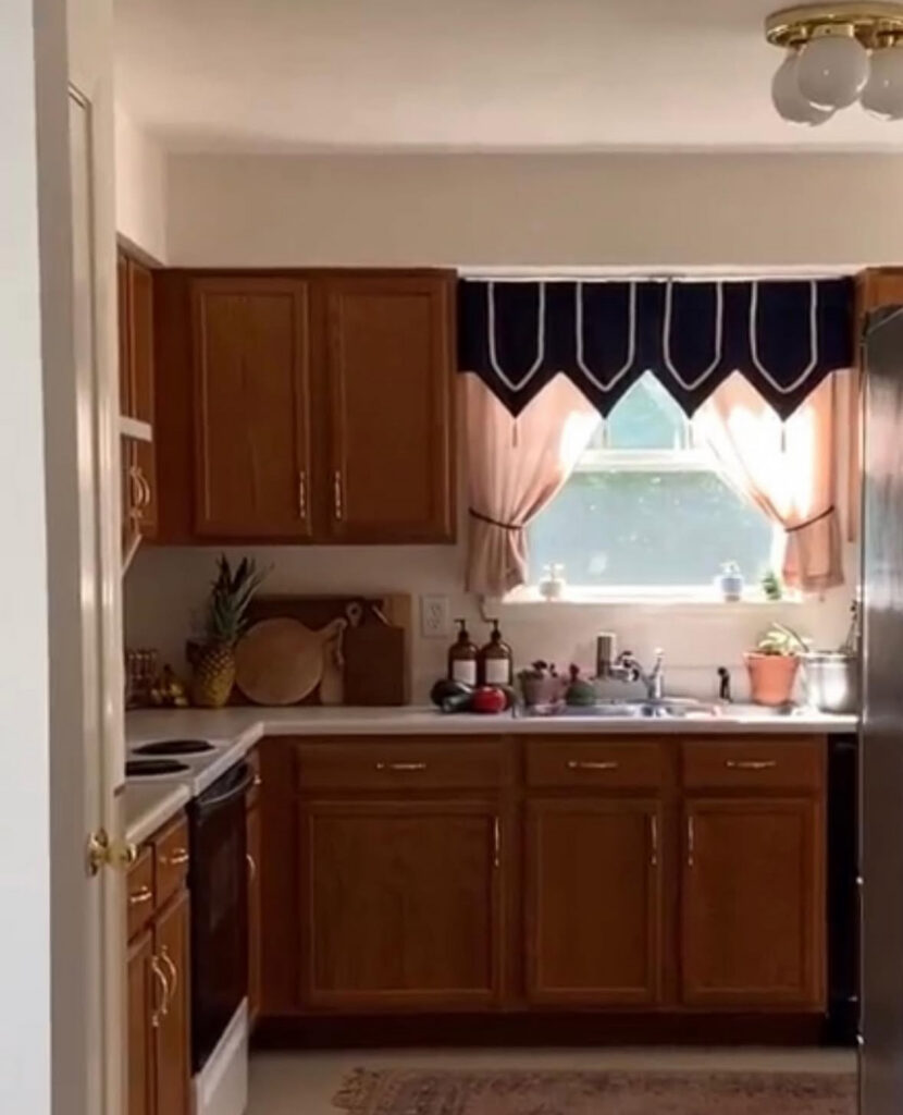Neutral kitchen with standard wood cabinets, beige tile and a heavy window valance before the update by @acarriedaffairdesigns.