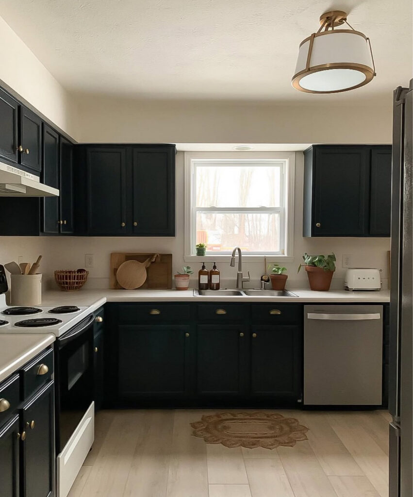 Modern kitchen with deep navy cabinets, brass hardware, light worktops and warm wood flooring created by @acarriedaffairdesigns.