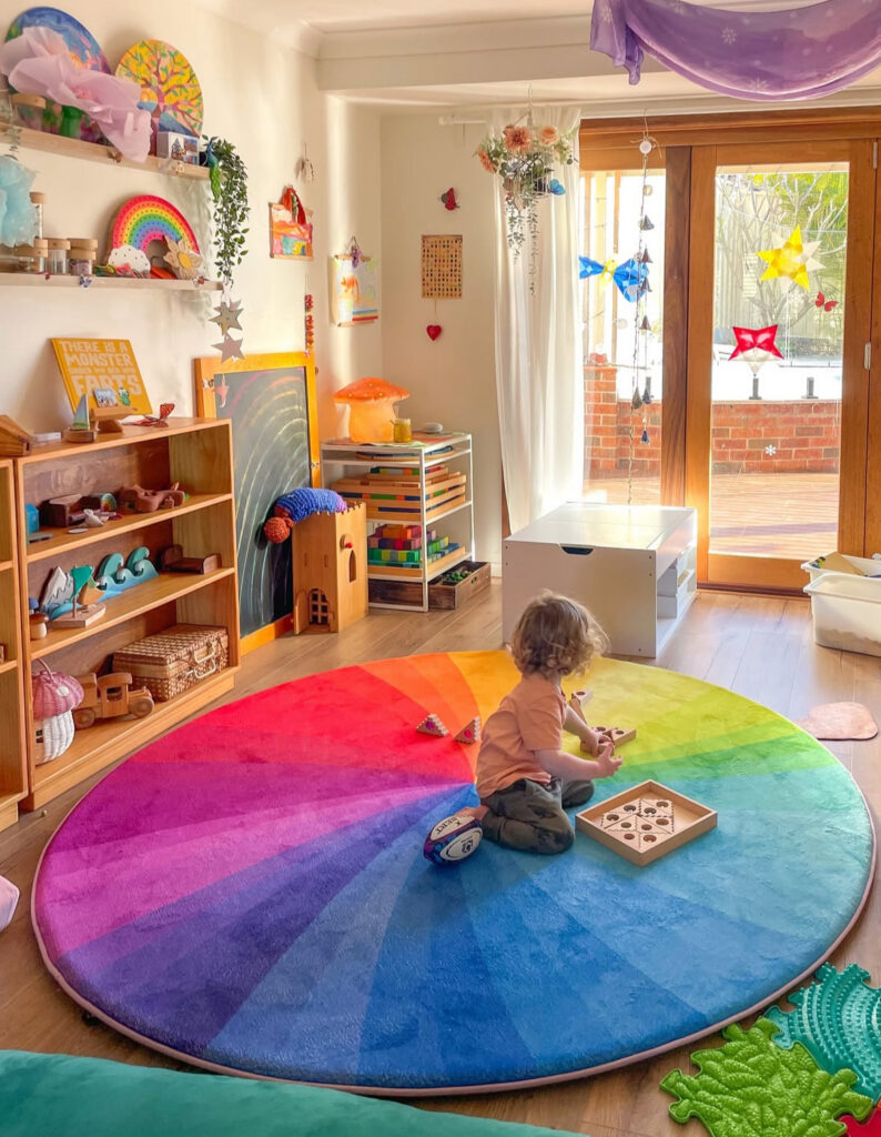 Bright round rainbow rug defining a central play zone in a sunny kids playroom.