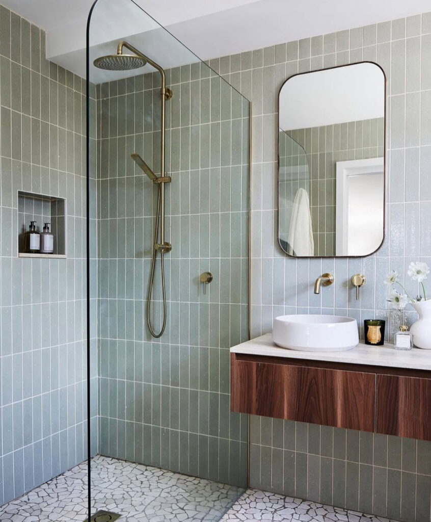 Relaxing green bathroom color scheme with sage tile walls, brass fixtures, and a floating walnut vanity for a modern look.