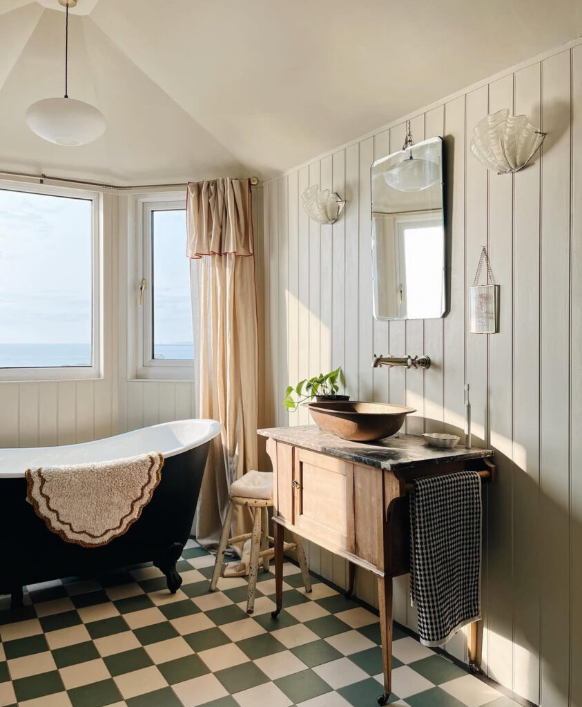 Sunlit coastal room showcasing vintage bathroom ideas with a green and cream checkered floor and freestanding tub.
