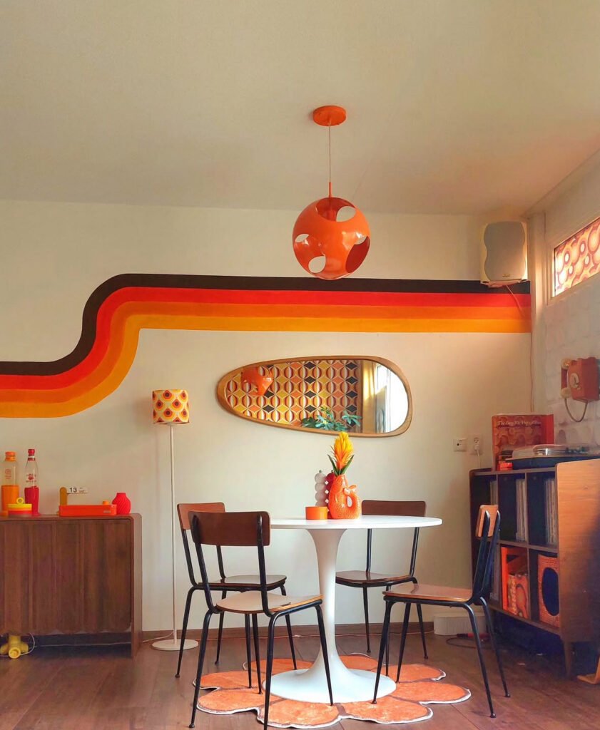 Playful retro 70s living room dining area with bold rainbow stripe mural, tulip table and vintage chairs.