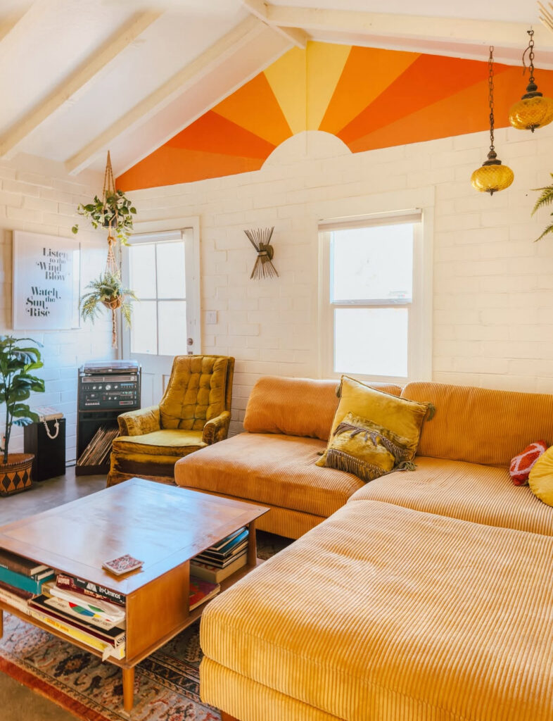 Cheerful 70s style living room decor with painted sunrise wall, mustard corduroy sectional and vintage stereo.
