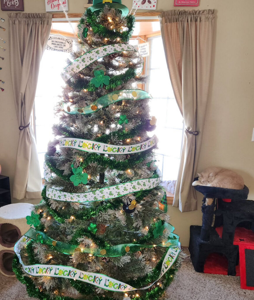 st pattys day tree with green ribbon, shamrocks, twinkle lights, and a very sleepy cat nearby.