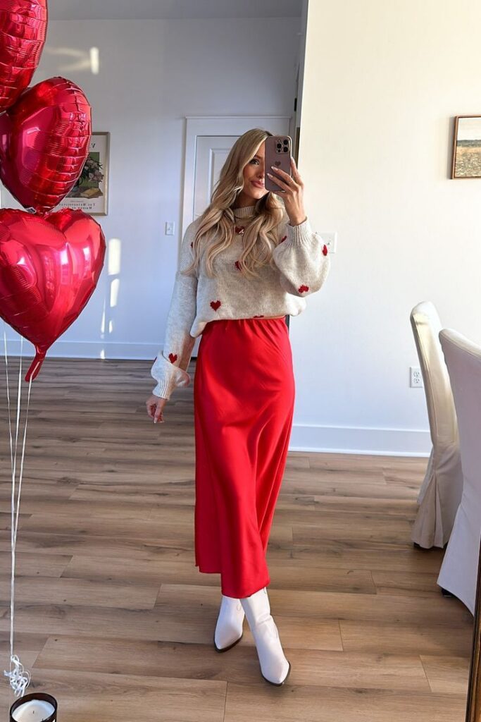 Valentines Day outfit: cream heart sweater with a red satin skirt and white boots (mirror selfie with heart balloons).
