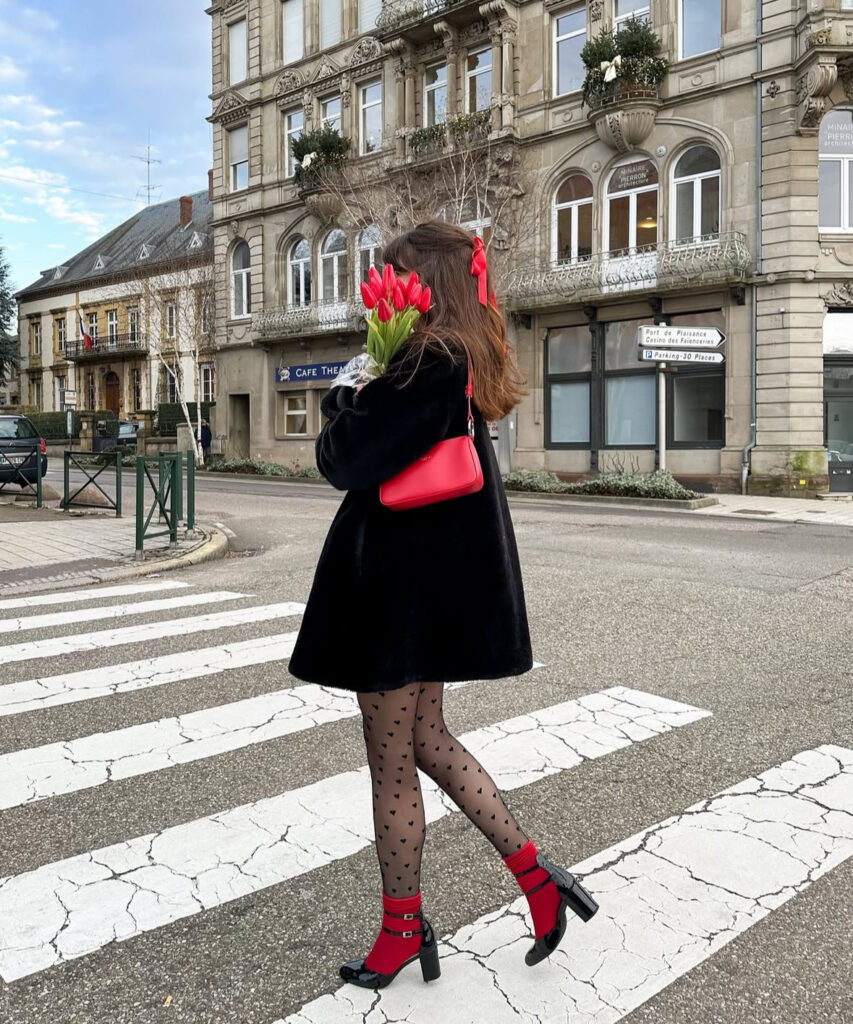 Cool-girl Valentines Day outfit: black coat with red heels and sheer polka-dot tights for a city-date vibe.