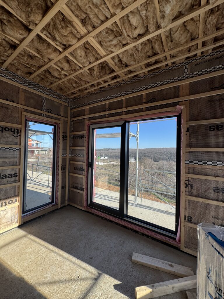 Interior view of anthracite frame sliding windows installed in a timber frame room with open countryside beyond