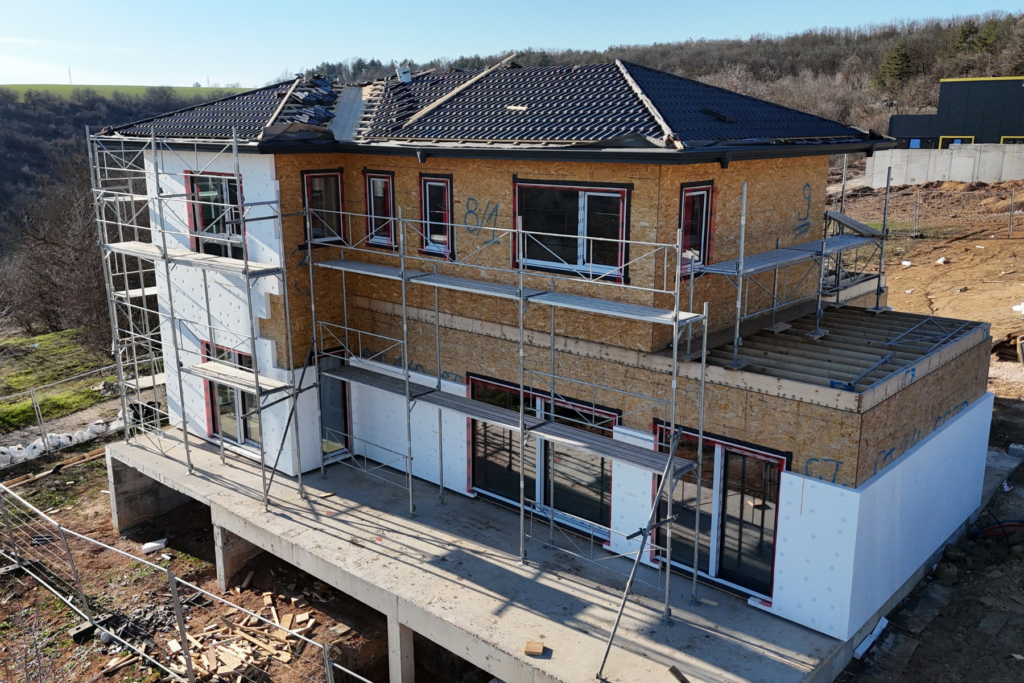 Side view of house under construction with new windows installed, dark roof, and scaffolding around the facade