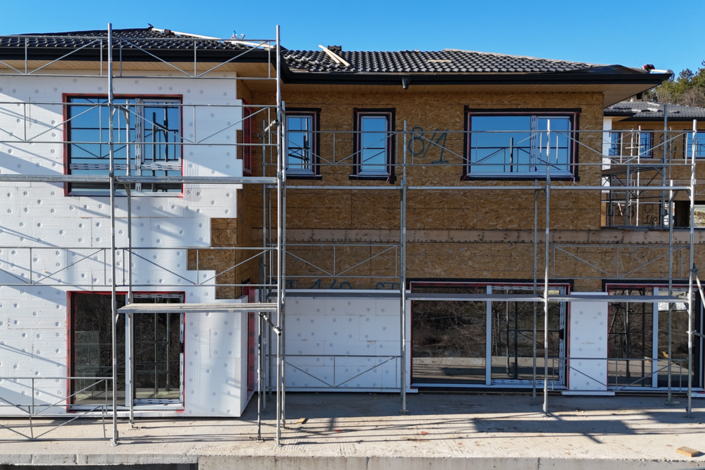 Front facade during window installation with scaffolding, mixed window sizes, and large picture windows in place