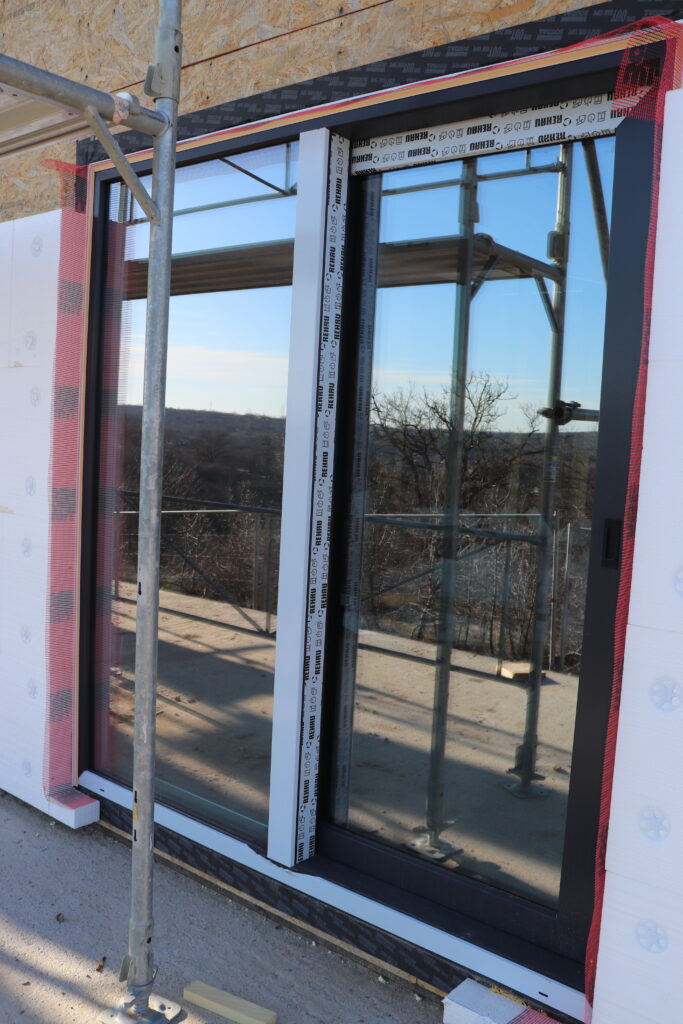 REHAU Synego Slide door installed with anthracite frame, exterior insulation, and visible airtight tape around the opening