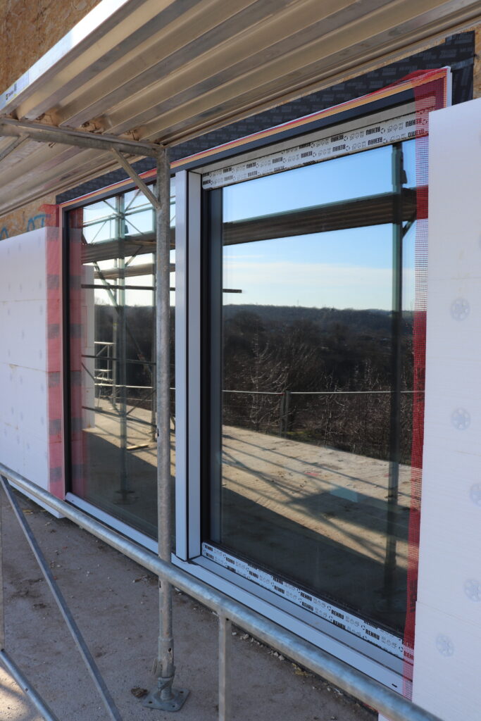 Large REHAU Synego Slide window installation with anthracite frame, exterior insulation, and pink airtight mesh tape at the edges