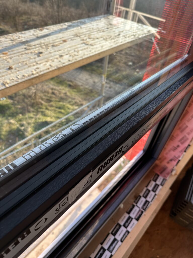 Close-up of black warm-edge spacer bar inside a triple-pane window with anthracite frame and airtight tape visible