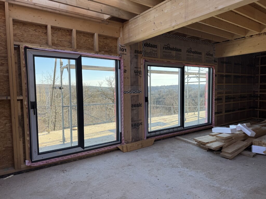 Large anthracite framed windows installed in an unfinished interior with taped airtight window-to-wall joints