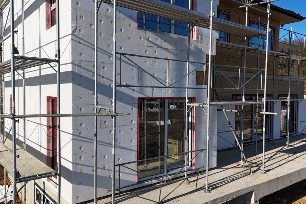House under construction with exterior insulation, scaffolding, and newly installed large windows and sliding doors