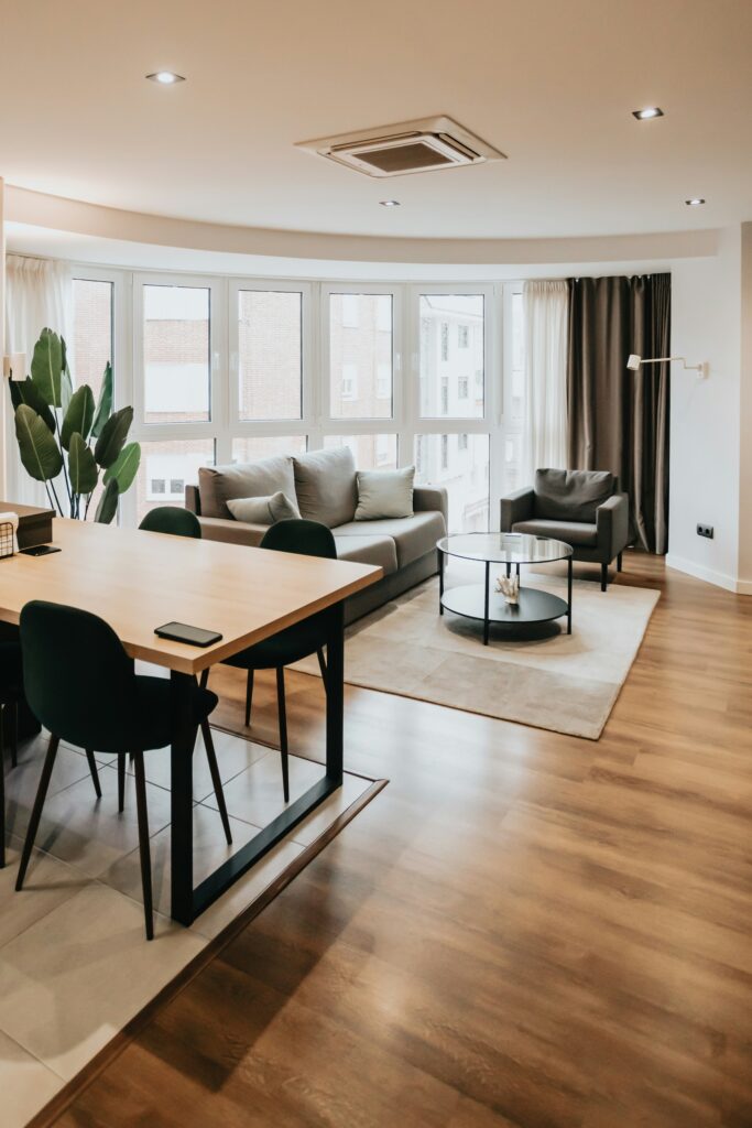 Modern apartment living room with a shallow tray ceiling, recessed lights, large windows, and neutral furniture