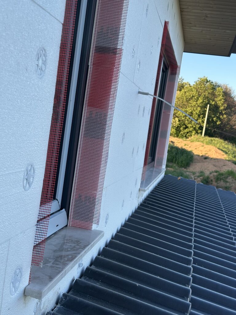 Limestone window sill on second floor of new build house with anthracite roof tiles and wooden soffit visible in background