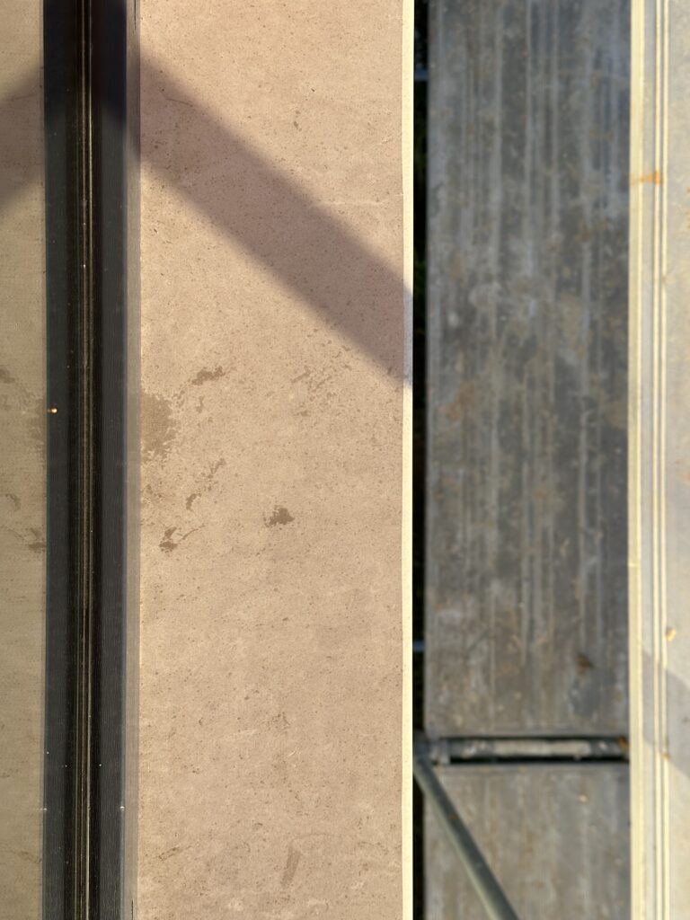 Close-up of limestone window sill texture showing natural warm beige tone and veining pattern next to dark window frame