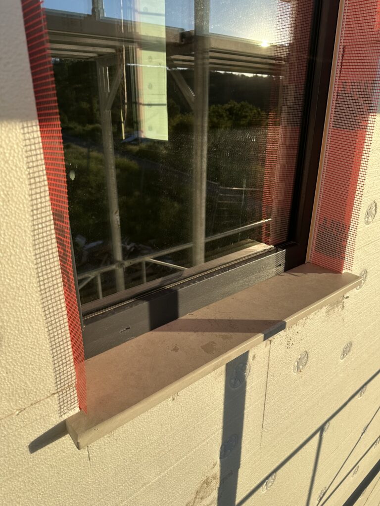 Front view of limestone exterior window sill installed on insulated facade with fiberglass mesh and mechanical anchors visible before plastering