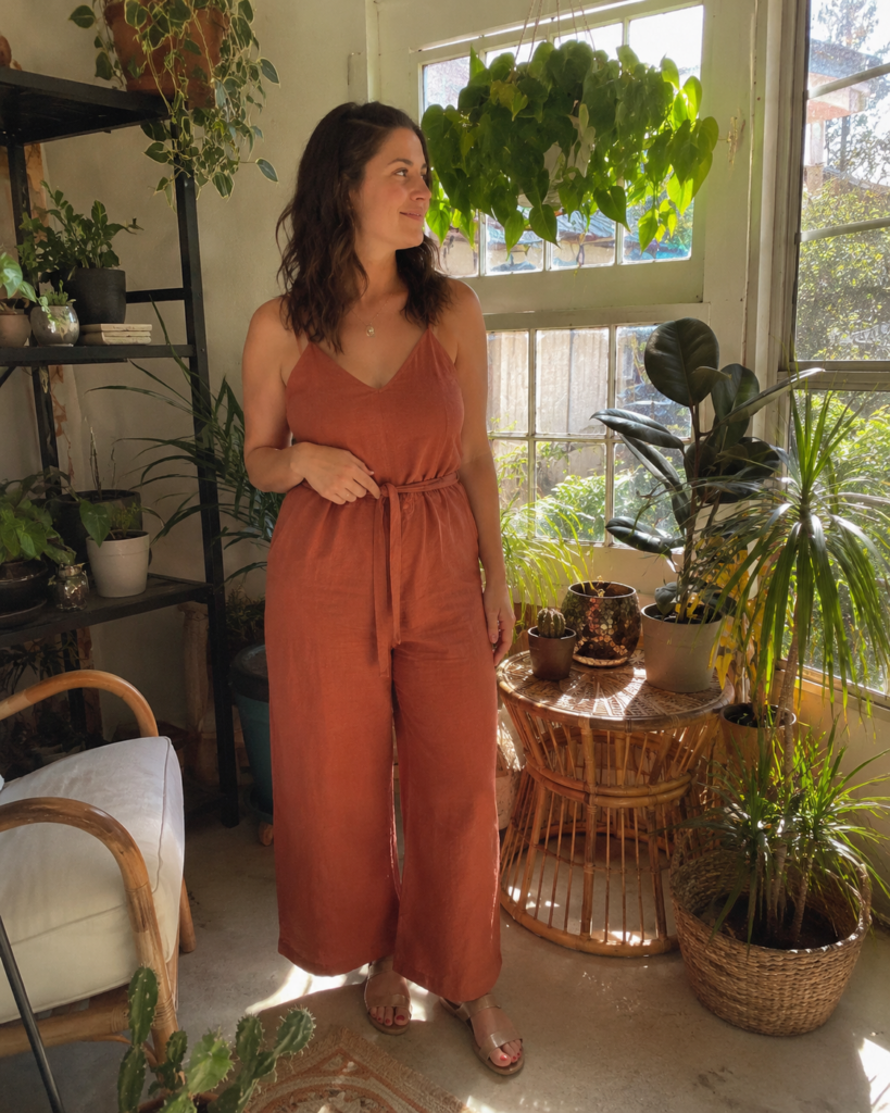 Woman in a belted terracotta linen jumpsuit and flat sandals in a sunroom, summer work outfit