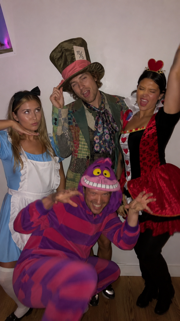 Mismatched group in blue dress, top hat, striped cat, and heart-print queen costumes, Alice in Wonderland Disney Halloween costume