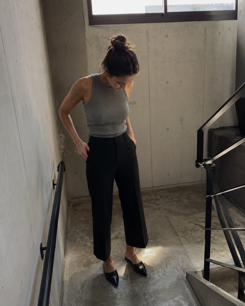 Woman in cropped black wide-leg trousers, grey ribbed tank, and mules on a stairwell, summer work outfit