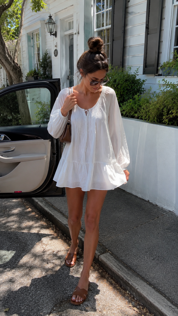 Woman wearing a loose white mini dress with brown sandals while stepping out of a car on a sunny street.