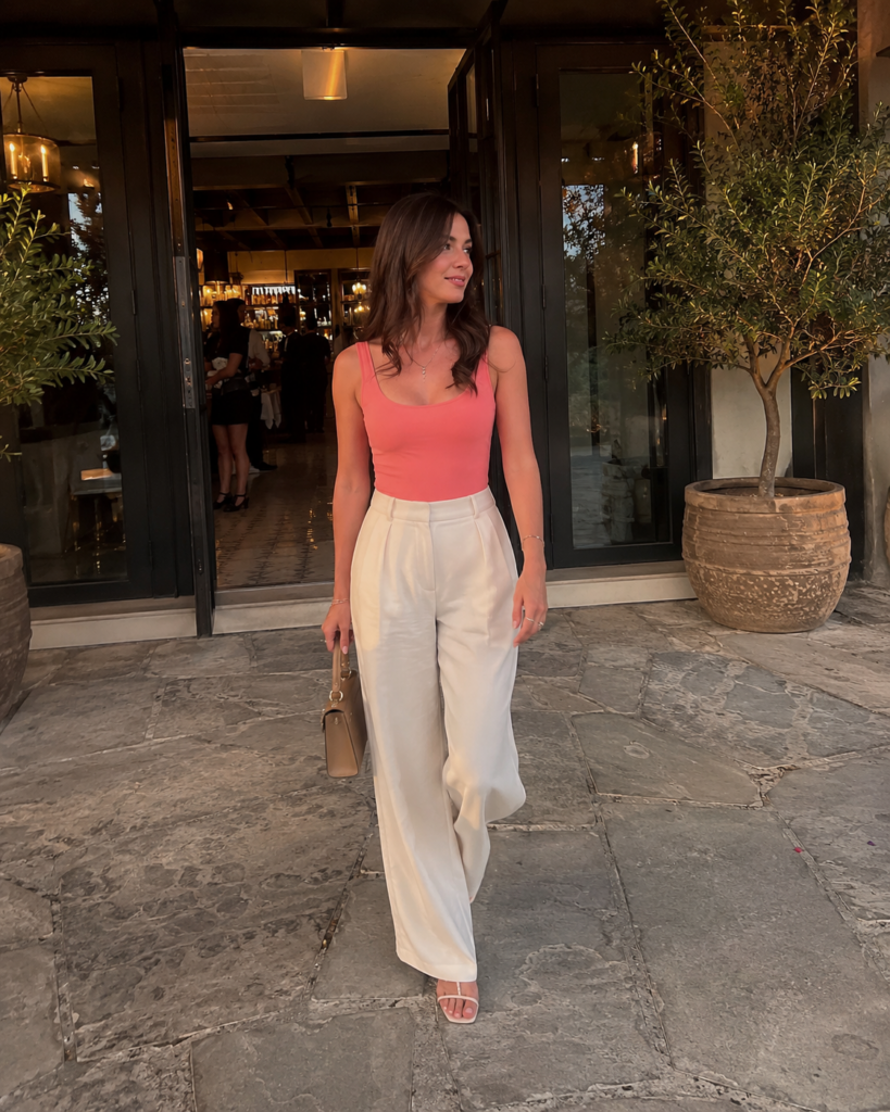 Soft coral sleeveless top styled with cream trousers and neutral sandals for a summer evening outfit.