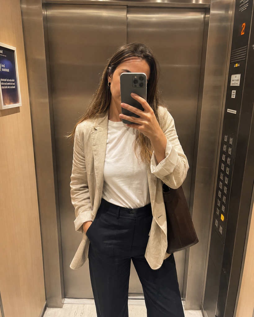 Woman in navy tailored trousers, white tee, and linen blazer in an office elevator, summer work outfit