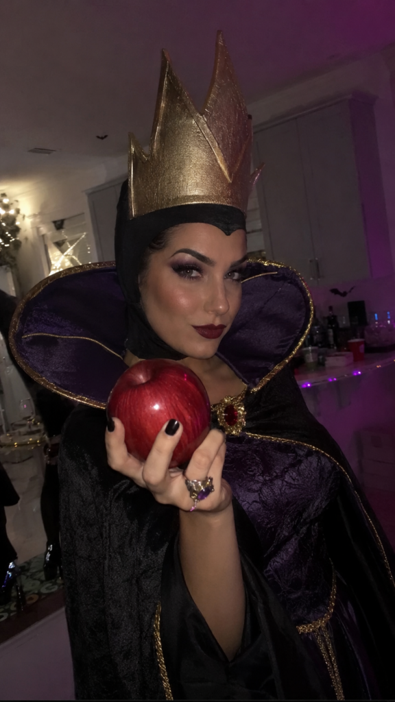 Woman in a dark regal gown with a tall collar holding a red apple, Evil Queen Disney Halloween costume